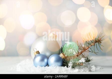 Beautiful Christmas balls with snow and fir tree branches on table against blurred lights Stock Photo
