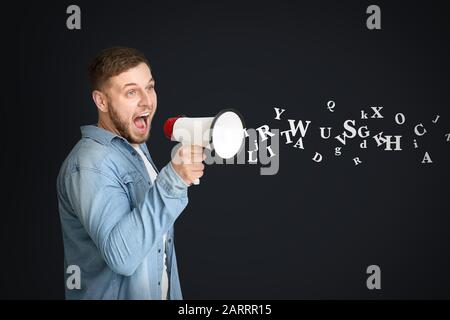 Young man with megaphone and many letters on dark background. Studying of foreign language Stock Photo