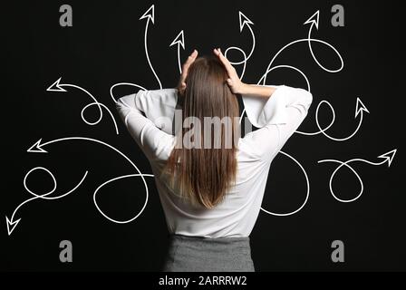 Stressed businesswoman and many arrows on dark background. Concept of choice Stock Photo