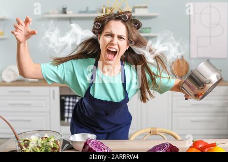 Aggressive young housewife with steam coming out of ears in kitchen Stock Photo