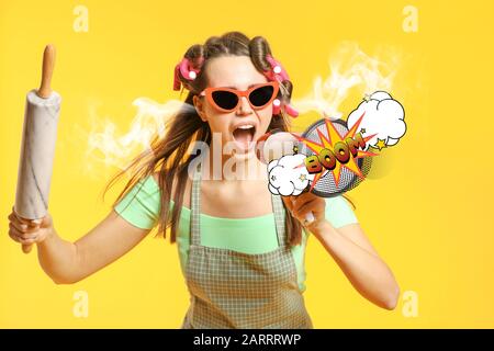 Funny housewife with steam coming out of ears, rolling pin and megaphone on color background Stock Photo