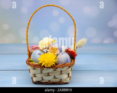 A basket with colored Easter eggs, decorated with dried flowers, on a wooden background. Stock Photo