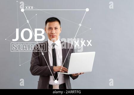 Asian man with laptop using job search site against grey background Stock Photo