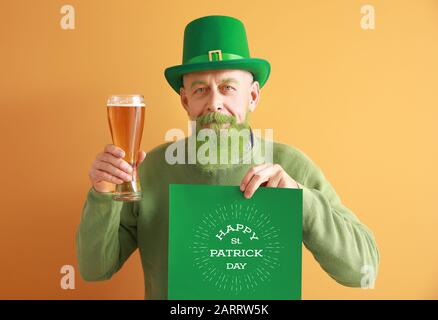 Funny mature man holding glass of beer and poster with text HAPPY ST. PATRICK'S DAY on color background Stock Photo