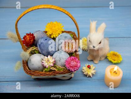 A basket full of Easter eggs painted blue, a hare, and burning candles Stock Photo