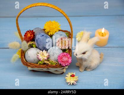 A basket full of Easter eggs painted blue, a hare, and burning candles Stock Photo