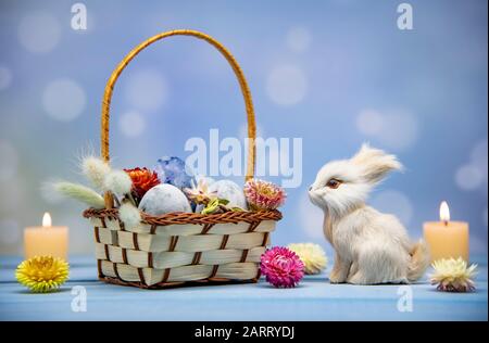 A basket full of Easter eggs painted blue, a hare and burning candles  Stock Photo