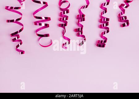 Curly shiny ribbons on pastel pink background. Stock Photo