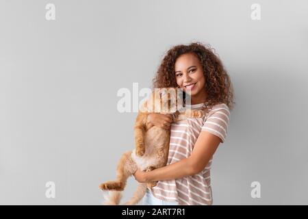 Young African-American woman with cute cat on light background Stock Photo