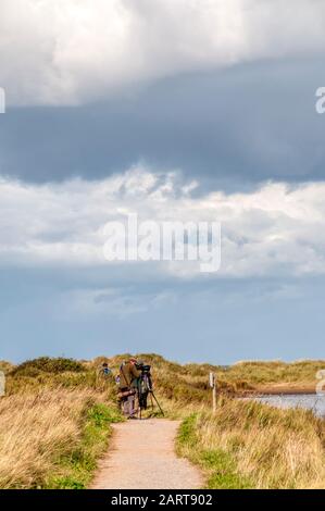 Bird watchers on the west bank path at the RSPB Titchwell Marsh bird reserve looking over the Tidal Marsh. Stock Photo