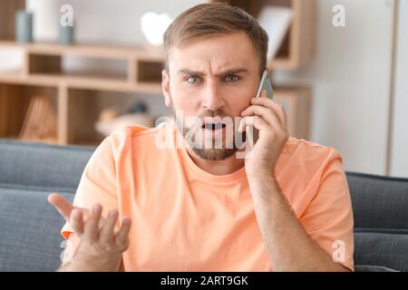Confused young man talking by phone at home Stock Photo