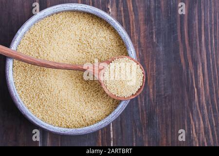 Dry couscous in a bowl and spoon on wooden background, Stock Photo