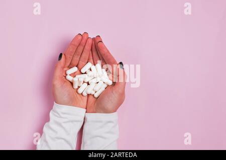 Woman's hand's holding a lot of white pills over pink background Stock Photo