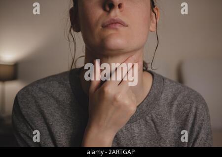 Sore throat, virus disease or flu. Woman holds hand against her throat feeling pain in bedroom Stock Photo