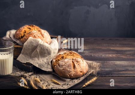 Homemade rustic rye bread with coriander seeds and a glass of milk on old wooden table. Rural food still life. Stock Photo