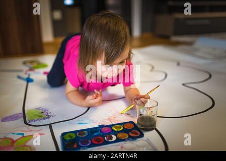 Two-year old girl paints with poster paintings indoors on the floor. Stock Photo
