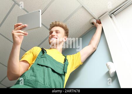 Electrician with tablet computer installing alarm system indoors Stock Photo