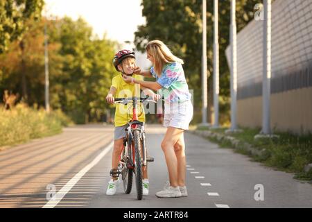 Mother helping her son to put on bicycle helmet outdoors Stock Photo