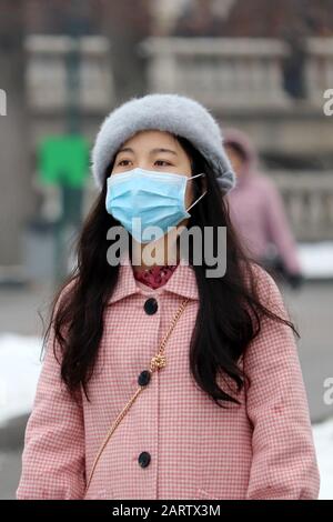 Coronavirus protection, chinese girl in protective medical mask standing on a winter city street in crowd, vertical shot Stock Photo