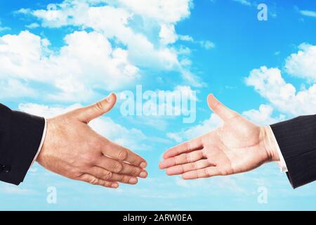 Two people hold out their hands for a handshake against the sky. The concept of the transaction Stock Photo