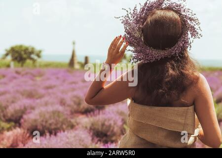 Girl in a dress and a wreath of lavender on her head who looks at the field. Beautiful girl in lavender wreath and retro dress on the lavender field o