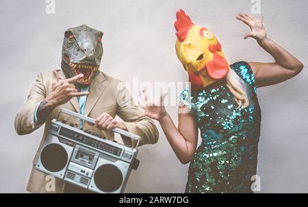 Crazy senior couple wearing chicken and t-rex mask while dancing outdoor - Mature trendy people having fun celebrating and listening music Stock Photo