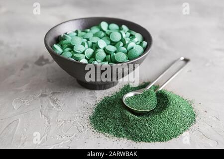 Bowl with spirulina pills and spoon with powder on table Stock Photo