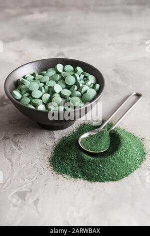Bowl with spirulina pills and spoon with powder on table Stock Photo
