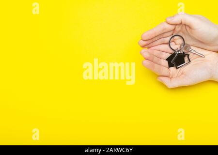 House keys with trinket in female hands on color background, top view with copy space. House key on yellow background. Minimal flat lay style with Stock Photo