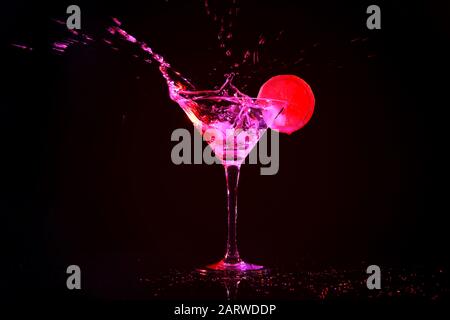 Dropping of ice cube into glass with tasty cocktail on dark background Stock Photo