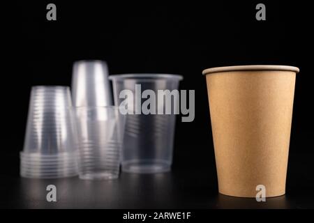 Plastic versus cardboard cups. Disposable tableware set on a table. Dark background. Stock Photo