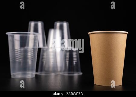 Plastic versus cardboard cups. Disposable tableware set on a table. Dark background. Stock Photo