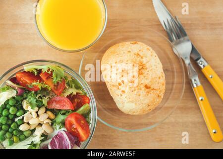 Tasty salad, glass of juice and bun for breakfast on table Stock Photo