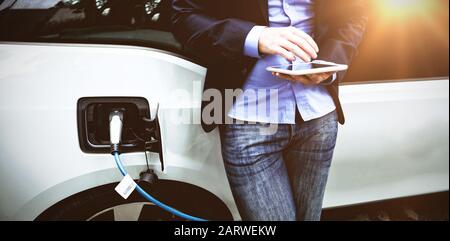 Businessman using digital tablet while charging electric car Stock Photo