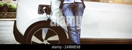 Businessman using digital tablet while charging electric car at charging station Stock Photo