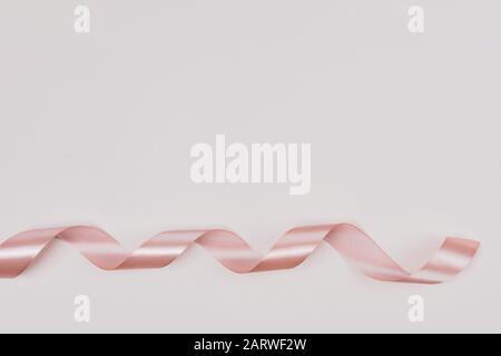 Perfect pink ribbon rolled on pale pink rustic background. Stock Photo