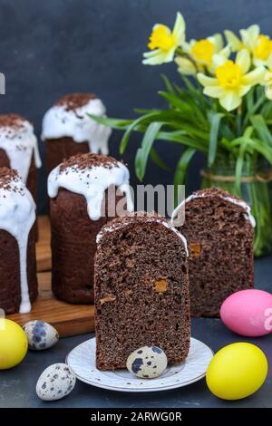 Still life with cut chocolate Easter cake and multi-colored Easter eggs on a dark background, Vertical orientation Stock Photo