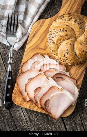 Sliced smoked ham. Tasty pork meat and bun on wooden cutting board. Top view. Stock Photo