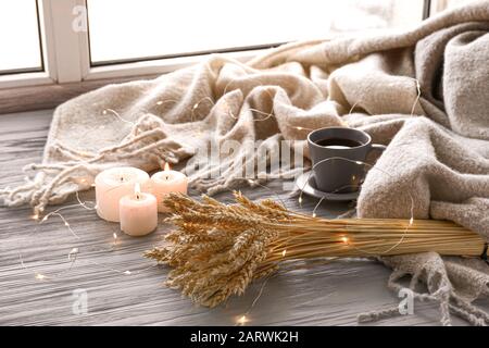 Christmas lights, burning candles, cup of tea and plaid on window sill Stock Photo