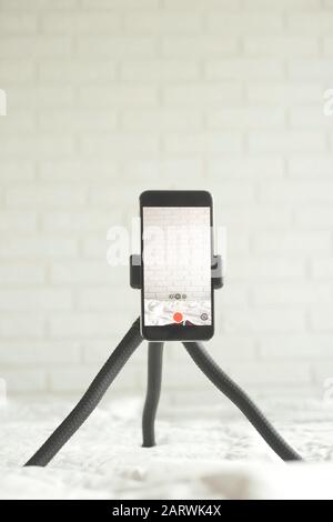 The smartphone stands on a compact tripod at home for recording video. Blogging tecnology concept. Stock Photo