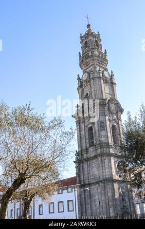 Tower of famous Clerigos Church in the historical center of Porto, Portugal. Baroque style church tall bell tower. Photographed from the adjacent park with trees. Vertical photo. Stock Photo