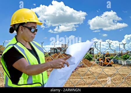 Female in construction looking over blue print in front of site. Stock Photo