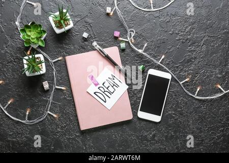Notebook, paper with text DREAM, mobile phone and pen on dark background Stock Photo