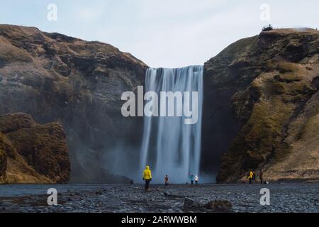 Skogafoss waterfall surrounded by people and rocks under a cloudy sky in Iceland Stock Photo
