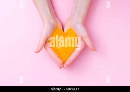 Orange slime in heart shape in kid hands. Girl hands playing slime toy on pink background. Making slime. Love and valentines day concept Stock Photo
