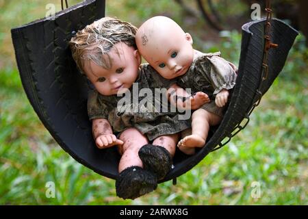Two Creepy Grungy Old Baby Dolls Sitting in a Tire Swing Stock Photo