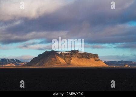 Field surrounded by rocks covered in the snow under a cloudy sky during the sunset in Iceland Stock Photo