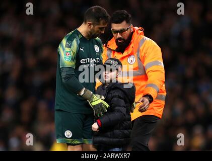 A young pitch invader is escorted off the pitch by Manchester City goalkeeper Claudio Bravo (left) and a steward during the Carabao Cup Semi Final, second leg match at the Etihad Stadium, Manchester. Stock Photo