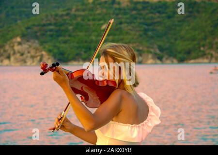 Beautiful woman playing violin at the sea with sunset background Stock Photo