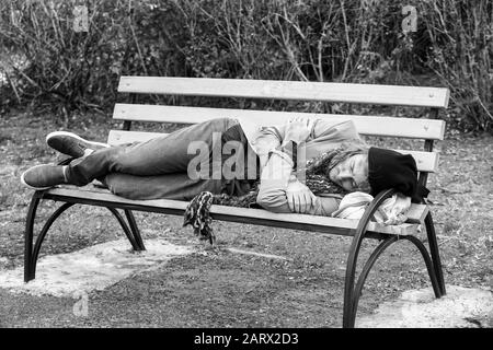 Black and white portrait of poor homeless man sleeping on bench outdoors Stock Photo